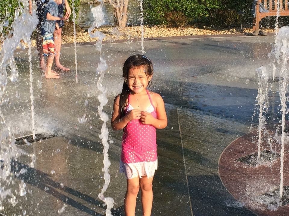 A little girl smiling at a play fountain in Sunset Island MD